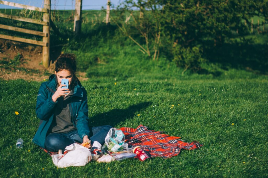 woman in blue outfit using blue smartphone while sitting on grass