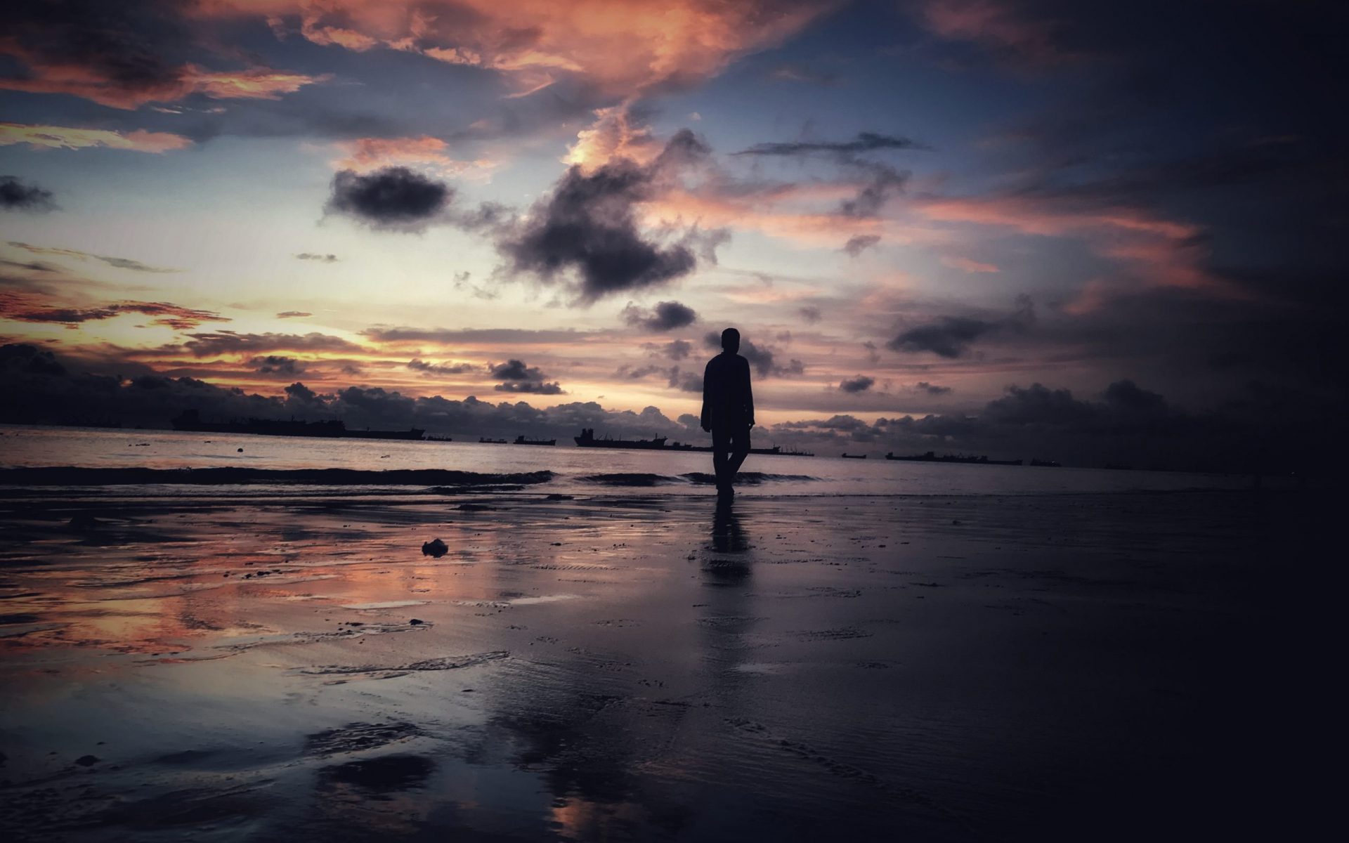silhouette of person standing on seashore during sunset