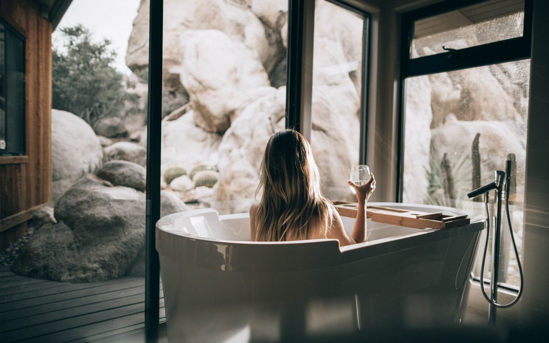 woman in white bathtub holding clear drinking glass